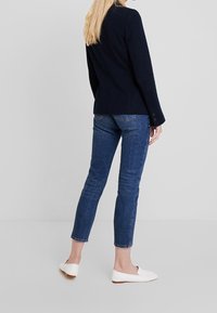 Granatowy blazer w paski z długimi rękawami, zestawiony z dopasowanymi niebieskimi dżinsami i białymi płaskimi butami. Blazer ma ozdobne guziki.