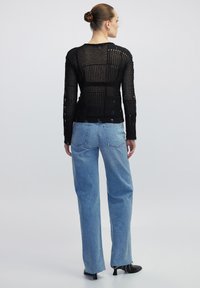 Haut en tricot noir à manches longues avec des motifs ajourés, associé à un jean droit bleu clair et des bottines à talons noires.