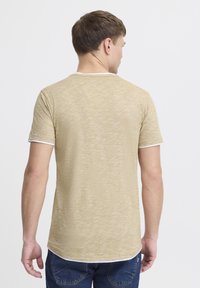 Tricou bej deschis cu un finisaj texturat, mâneci scurte și accente albe la guler și la tivurile mânecilor. Văzut din spate.