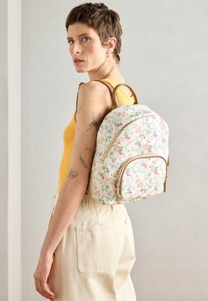 Floral-patterned backpack with cream base and brown accents; zip closure, rounded shape, adjustable straps, and front pocket.