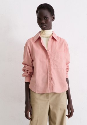 Light pink button-up shirt with a pointed collar, single chest pocket, and rolled-up sleeves, paired with beige wide-leg trousers.