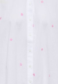 Chemise blanche à boutons avec de petits cœurs roses brodés éparpillés sur le tissu.