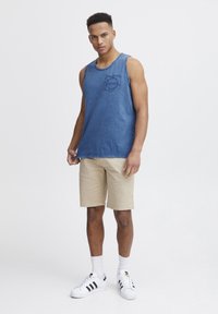 Blå denim tanktop med en frontlomme; parret med beige shorts og hvide sneakers med sorte striber. Hvide sportstrømper synlige.