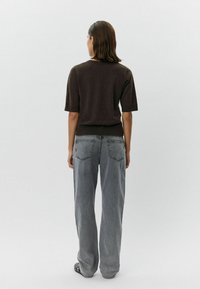 Brown short-sleeve top with a relaxed fit, paired with loose, faded gray jeans featuring two back pockets and a straight leg design.