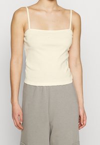 Ljusbeige linne med tunna axelband, figursydd design, gjort av mjuk bomull, med en liten Nike-logga på bröstet.