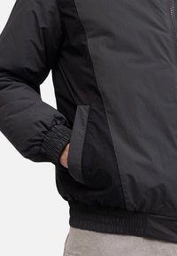 Giacca nera leggera con chiusura a zip, polsini elasticizzati e tasche laterali. Tessuto morbido con un taglio casual.