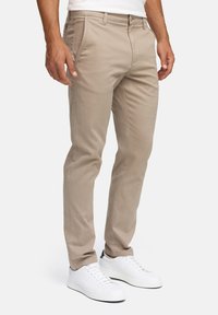 Beige katoenen chino's met een rechte pasvorm, voorzien van voorzakken en riemlussen, gecombineerd met witte veterschoenen.