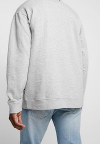 Sweat-shirt gris à manches longues avec des poignets côtelés. Présente un col rond et une coupe légèrement ample, associé à un jean bleu clair.