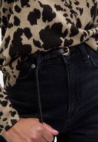 Maglione beige con stampa leopardata nera, abbinato a jeans neri. Una elegante cintura nera con fibbia dorata arricchisce l'outfit.