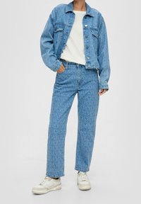 Giacca in denim blu chiaro e jeans abbinati con un motivo sottile. Maglione lavorato a maglia bianco sotto. Modello che indossa sneakers bianche.