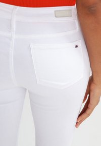 Valkoiset denim-farkut, joissa on istuva muotoilu, takataskut, pieni logotehoste ja sileä pinta.