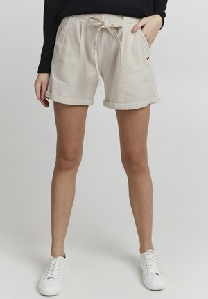 Beige linnen shorts met een trekkoord in de taille, opgerolde mouwen en zijzakken, gecombineerd met witte sneakers. Zachte textuur, casual ontwerp.