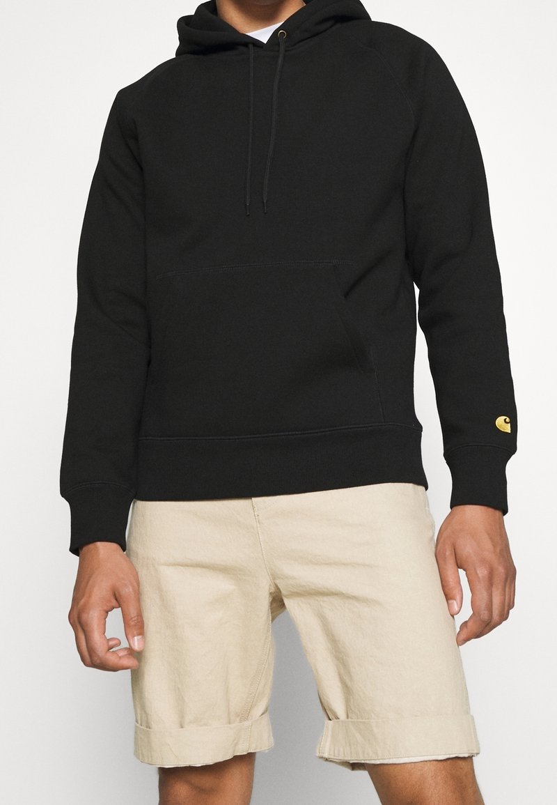 Svart hoodie tillverkad av mjukt tyg, med en framficka och ribbade cuffs. Den vänstra ärmen har en liten gul logotyp.