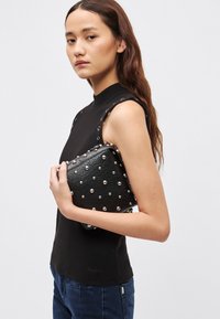 Mustast nahast käekott metallist naeltega, ristkülikukujuline, hoitakse musta varrukateta topi vastu. Sile tekstuur ja läikivad rõhutused.