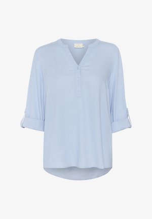 Svetlo modrá, dlhá košeľa s výstrihom do V, zapínaním na gombíky a vyrolovanými manžetami. Hladká látka s zaobleným spodným okrajom a voľným strihom.