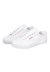 Sneakers bianchi in canvas con punta tonda, superficie texturizzata, sei occhielli, suola in gomma e un piccolo logo rosso sul lato.