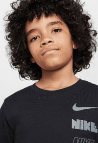 Fekete, rövid ujjas pamut póló, szürke Nike logóval és felirattal, kerek nyakkivágással és diszkrét texturált mintával.