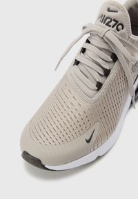 Baskets Nike Air 270 beige avec tige en maille, logos Swoosh noirs, semelle coussinée et lacets noués, vues de face et de côté.