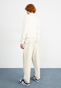 Sweatshirt off-white e calças cargo creme, apresentando um corte solto, bolsos traseiros e sapatilhas contrastantes com detalhes em azul marinho e branco.