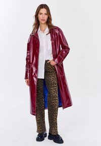 Dlhý vínovočervený lesklý vinylový kabát s prešitím, skombinovaný s nohavicami s leopardím vzorom a čiernymi platformami. Pod ním biela košeľa.
