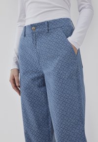 Džínové kalhoty v světle modré barvě s jemným propleteným vzorem, s rovnými nohavicemi, dvěma bočními kapsami a předním zapínáním na knoflík.