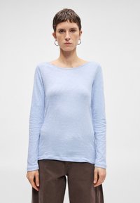 Svetlomodrá blúzka s dlhým rukávom a voľným strihom. Má široký lodičkový výstrih a textúrovanú látku. Kombinovaná s hnedými nohavicami širokého strihu.