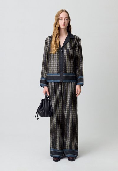 Completo in seta nera a motivo con pantaloni larghi e camicia con bottoni, con accenti blu e una borsa a secchiello nera con sottili righe bianche.