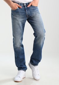 Blå denimjeans med en urtvättad finish, rak bendesign, femfickorsstil och knappstängning. Matchas med vita sneakers.