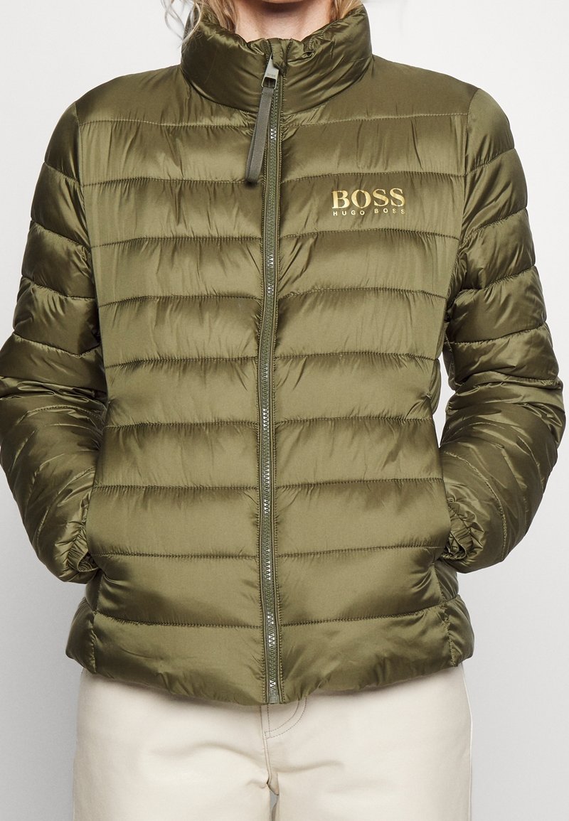 Chaqueta acolchada verde oliva con cuello alto, cremallera frontal, bolsillos laterales y el logo dorado "BOSS HUGO BOSS" en el pecho.