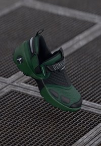 Groene en zwarte sportieve schoenen met een gestructureerde bovenkant, gewatteerde kraag en reflecterende accenten. Voorzien van een klittenband om een veilige pasvorm te garanderen.