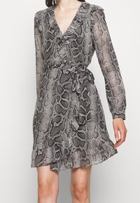 Schwarz-weiße Schlangenprint-Kleid mit langen Ärmeln, V-Ausschnitt, gebundenem Taillenbund und gerüschtem Saum, aus leichtem Stoff gefertigt.