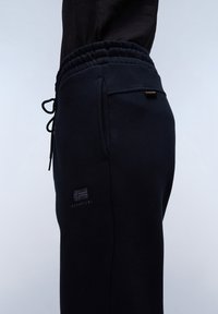 Dunkelblaue Jogginghosen mit einem Kordelzugbund, weicher Textur, Seitentasche und einem kleinen Logopatch mit einer Flagge.