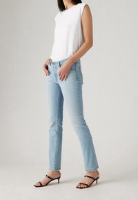 Vaqueros de color azul claro con corte recto, combinados con una blusa sin mangas blanca. Unos zapatos de tacón negro con tiras completan el atuendo casual.