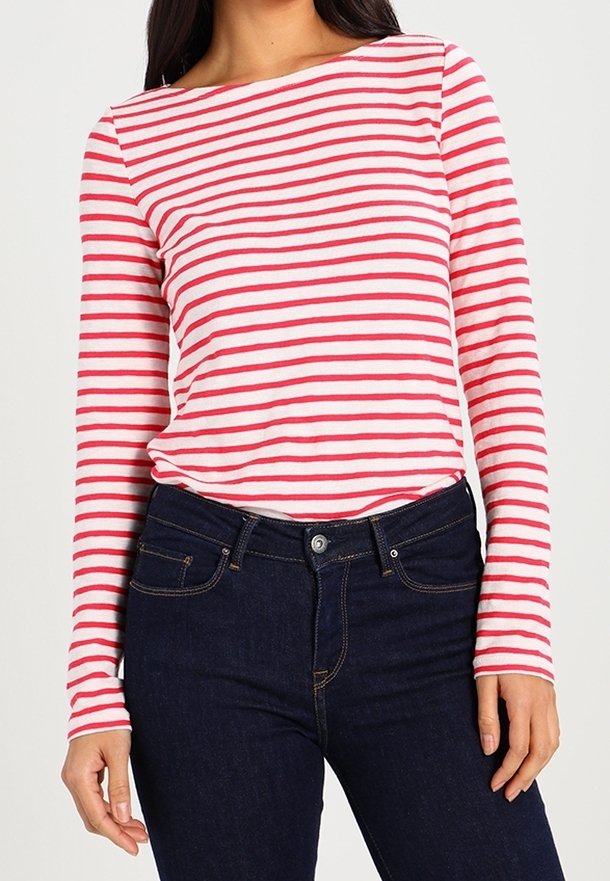 Camicia a righe rossa e bianca a maniche lunghe con scollo a barca, abbinata a jeans in denim blu scuro. La texture è morbida e aderente.