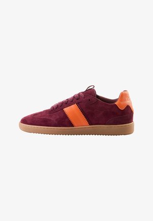Burgundy suede sneakers with an orange stripe, rounded toe, lace-up design, and gum rubber outsole. Rear has logo detail on the heel.