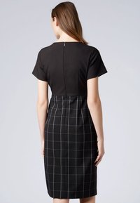Černé šaty s krátkými rukávy, přiléhavým korzetem a tužkovou sukní s bílou mřížkovou strukturou. Zapínání na zip na zadní straně.