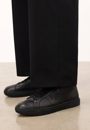 Zapatillas de cuero negro con una textura suave, que cuentan con una suela de goma, diseño con cordones y un sutil detalle de logo tonal en el lateral.