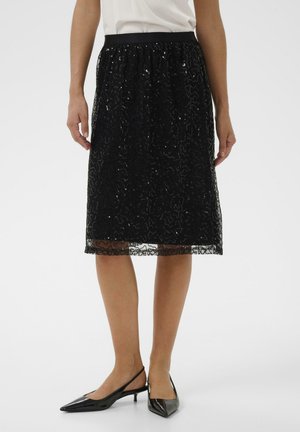 Schwarzer knielanger Rock mit strukturiertem Spitzenüberzug und kunstvollen Mustern, elastischem Taillenbund und durchsichtigen Saum. Kombiniert mit schwarzen Slingback-High Heels.