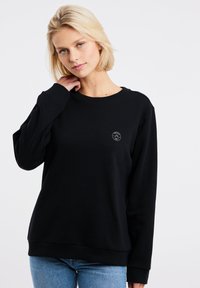 Zwarte crewneck sweatshirt gemaakt van een zachte stof, met een klein rond logo op de borst. Lange mouwen en een relaxte pasvorm.