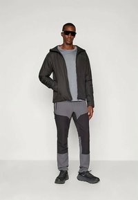 Black lightweight jacket, gray T-shirt, and black-gray patterned pants. Accessories include black sunglasses and black athletic shoes.