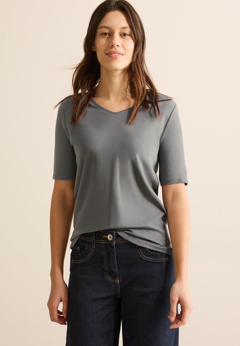 T-shirt grigia a maniche corte con scollatura a V, texture liscia e vestibilità comoda, abbinata a jeans in denim blu scuro con cuciture a contrasto.