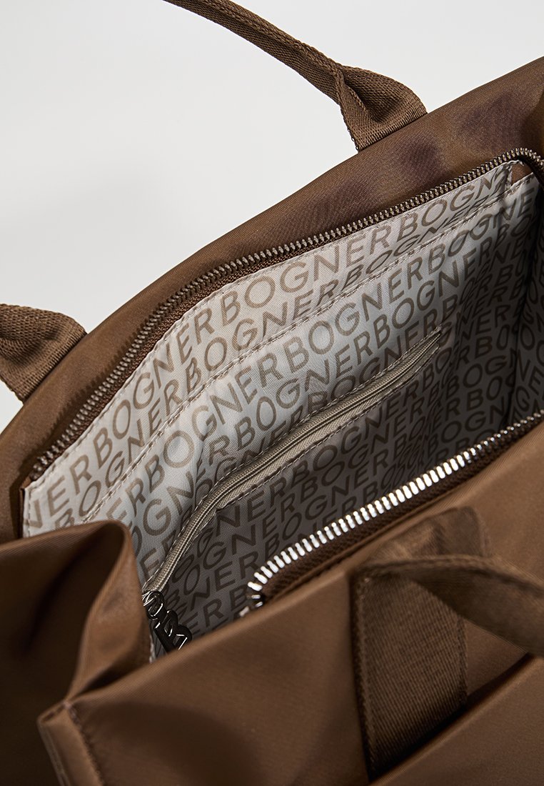 Braune Stofftasche mit zwei Griffen, Reißverschlussverschluss und einem gemusterten Innenfutter, das den Markennamen in hellgrau auf einem beigen Hintergrund zeigt.