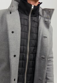 Grå uldblandingsfrakke med en sort quiltet inderside, der har en høj krave, lynlåslukning og knapdetaljer.