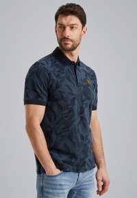 Polo bleu marine avec un motif de feuilles subtil, à manches courtes et col noir. Présente un petit patch de marque sur la poitrine.