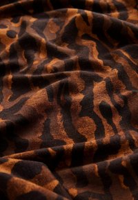 Hnedá a čierna tkanina s pruhovaným vzorom tigra, s hladkou textúrou a mierne pokrčeným vzhľadom.