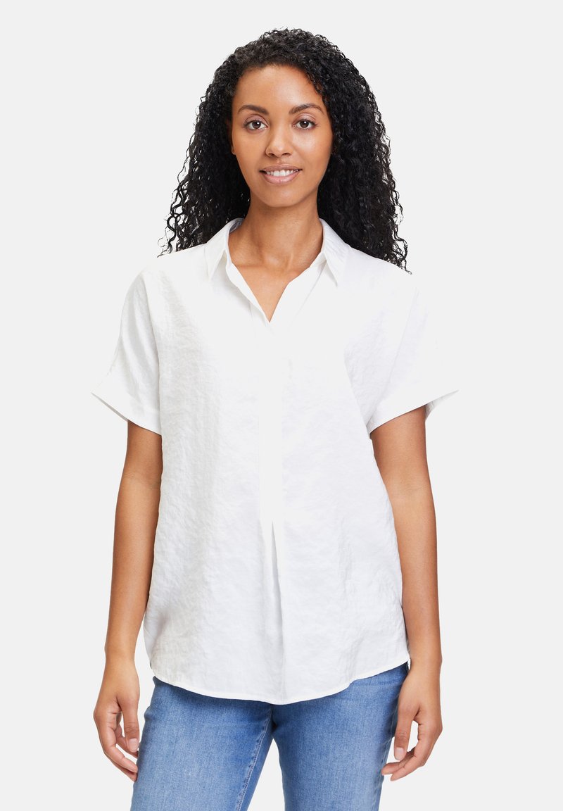 Weißes, kurzärmliges Hemd aus strukturiertem Stoff mit durchgehender Knopfleiste und lockerer Passform. Kombiniert mit hellblauen Jeans.