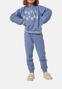 Modrý bavlněný svetr s nápisem "PETIT BATEAU" béžovými písmeny, doplněný o odpovídající modré tepláky se žebrovanými manžetami a pasem.