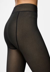 Leggings pretos de cintura alta com uma textura suave e elástica. Apresenta uma faixa de cintura reforçada e detalhes de costura discretos ao longo das costuras.