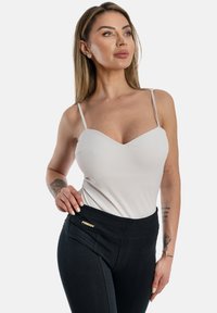 Top senza maniche di un grigio chiaro con scollatura a V, abbinato a leggings neri a vita alta in tessuto testurizzato con un accento del logo dorato.