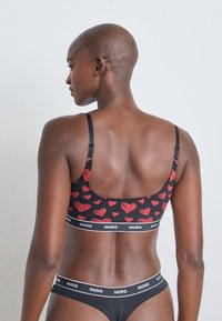 Svart bralette med rødt hjerte mønster, justerbare stropper og en merkebånd. Glatt stoff med en fitted, komfortabel design.